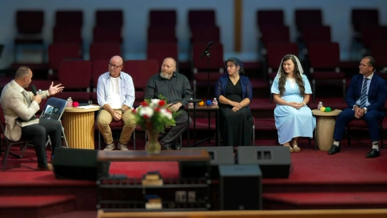 The Real Talk About Relationships panel on stage at Morning Star Christian Church in Boise, Idaho — a pastor with a microphone asking a question while five panelists, including two married couples, listen from the platform
